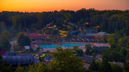 Aerial view of a water park at sunset, featuring colorful water slides and a swimming pool surrounded by trees.