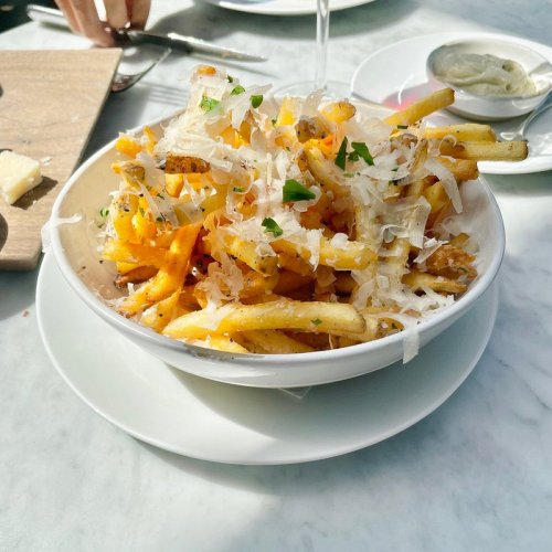 A bowl of golden fries topped with grated cheese and herbs, served on a white plate.