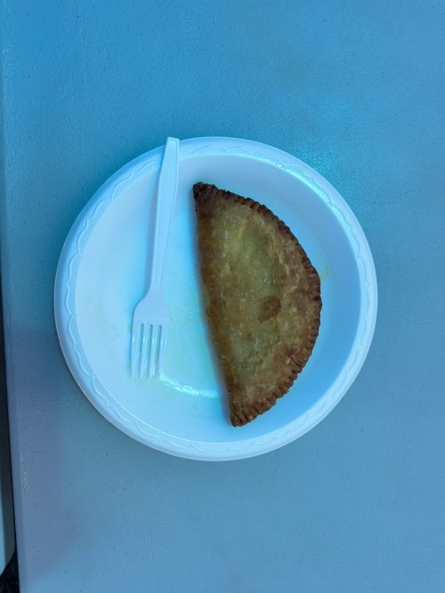 A half-eaten fried pastry on a white plate with a plastic fork beside it.