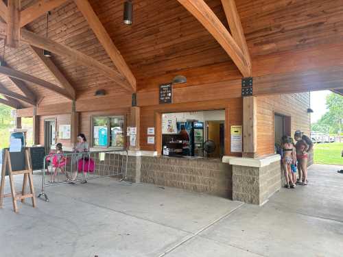 A wooden pavilion with a service window; people waiting in line and others seated nearby.