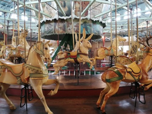 A vintage carousel featuring intricately carved animals, including a horse and a rabbit, in a colorful setting.