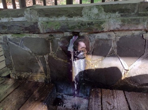 A stone structure with water flowing from a crack, creating a small stream on a wooden surface.