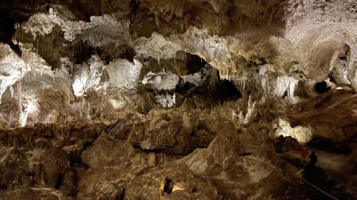 A dimly lit cave interior with intricate rock formations and stalactites hanging from the ceiling.