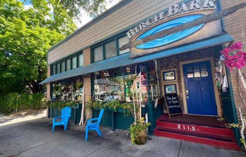 A charming storefront with blue chairs outside, featuring a sign that reads "Birch Bark" and a welcoming entrance.