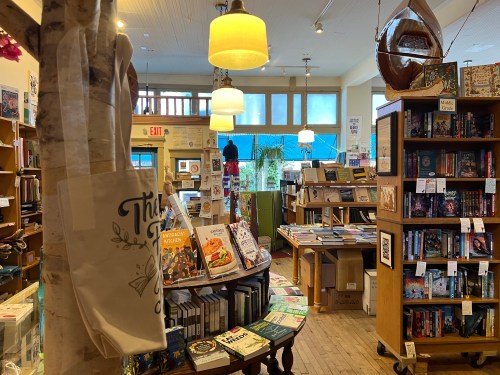 A cozy bookstore interior with wooden shelves, books, and warm lighting, featuring a display table in the center.