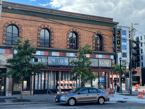 Historic brick building with a marquee, trees in front, and construction barriers on the street.