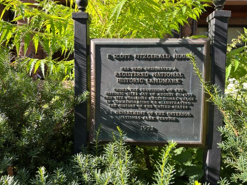 Plaque for the F. Scott Fitzgerald House, designating it as a registered national historic landmark, surrounded by greenery.