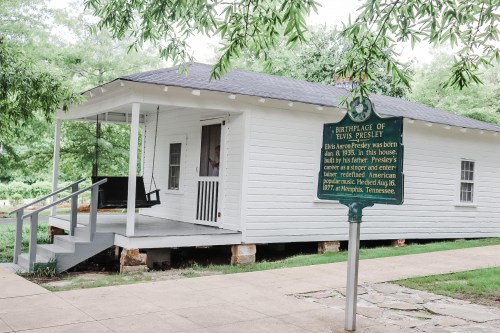 Historic white house with a sign reading "Birthplace of Elvis Presley," surrounded by greenery.