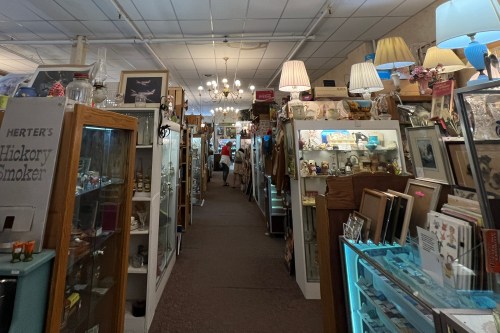A narrow aisle in an antique shop lined with display cases and vintage items, illuminated by overhead lights.