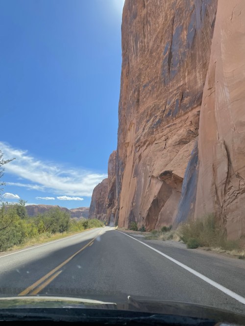 A scenic view of a road winding through towering red rock formations under a clear blue sky.