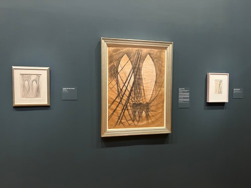 Three framed artworks displayed on a dark wall, featuring abstract designs in neutral tones.