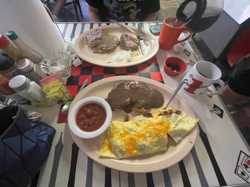 Two plates of breakfast: one with an omelet and salsa, the other with steak and beans, alongside coffee and condiments.