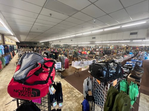 A spacious retail store filled with clothing, bags, and outdoor gear, showcasing a variety of products on display.