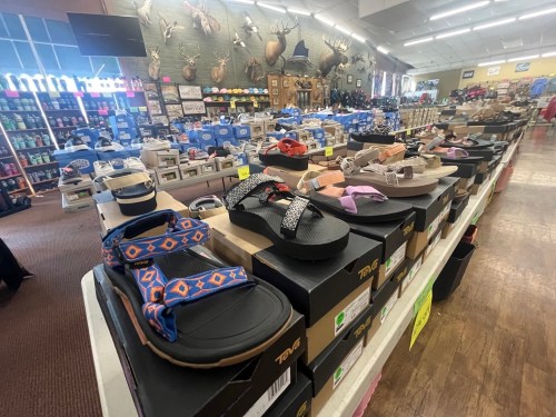 A display of various sandals and shoes in a retail store, with shelves and merchandise in the background.