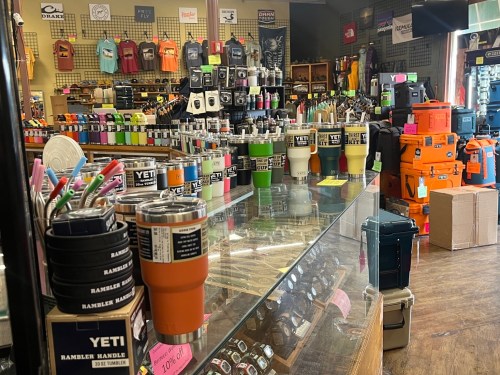 A display of various YETI cups and outdoor gear in a retail store, with colorful products arranged on shelves.