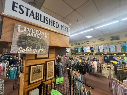 Interior of a retail store featuring clothing displays, a sign reading "Established 1953," and a "Live Oak Brand" sign.