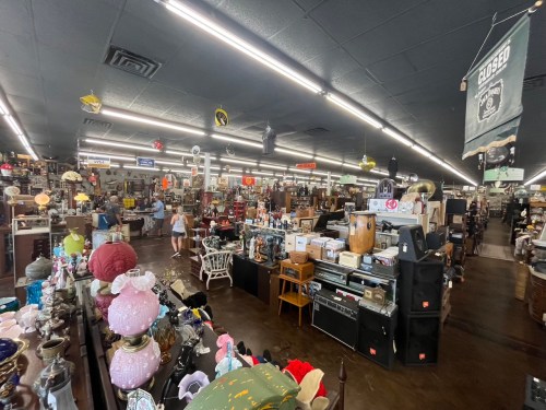 A spacious antique store filled with various vintage items, furniture, and decor, with shoppers browsing around.