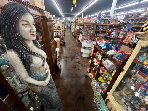 A wide aisle in an antique store filled with various collectibles and a large wooden statue of a woman on the left.