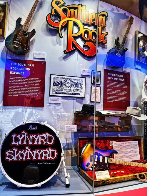 Display case featuring Southern Rock memorabilia, including guitars, a drum, and informative plaques.