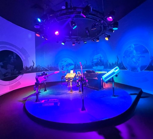 A vibrant music studio setup with colorful lights, featuring guitars, keyboards, and electronic instruments.