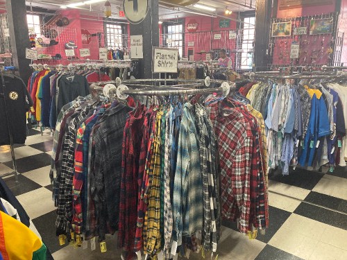 A clothing rack filled with various flannel shirts in a vibrant store with a checkered floor.