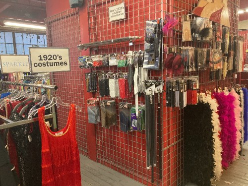 A display of 1920s costumes and accessories on a red grid wall in a costume shop.