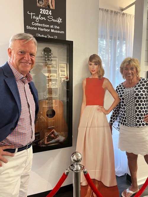 A man and woman pose beside a life-size cutout of Taylor Swift at a museum exhibit featuring her collection.