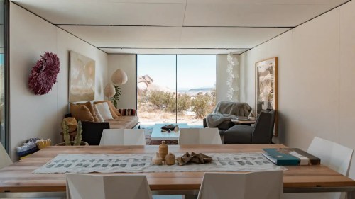 Modern interior of a bright living space with a dining table, cozy seating, and large windows showcasing a desert view.