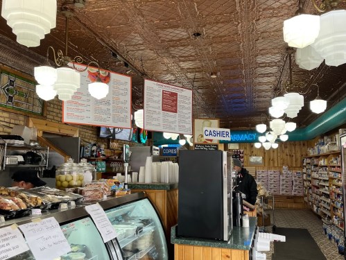 A cozy café interior with a menu board, display cases, and a cashier area, featuring vintage lighting and wooden accents.