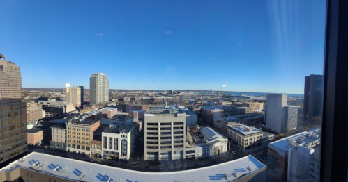 A panoramic view of a city skyline on a clear day, featuring buildings and a distant waterfront.