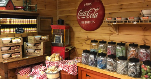 A cozy shop interior with wooden walls, jars of candy, a popcorn machine, and Coca-Cola signage.