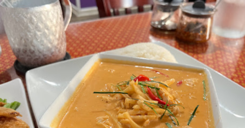 A bowl of creamy curry with shredded vegetables, served with a side of rice on a patterned table.