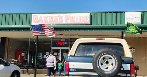 A bakery named "Baker's Pride" with an open sign, American and green flags, and customers outside.