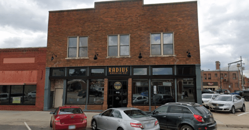 Exterior view of Radius Brewing Co. building with large windows and parked cars in front.