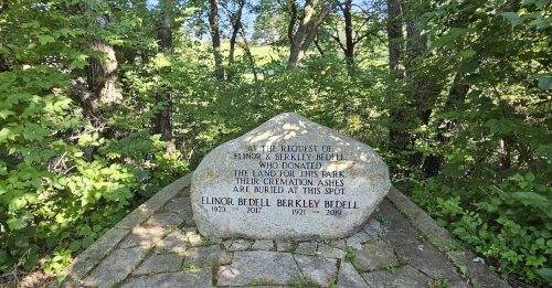 A stone memorial in a wooded area honoring Elinor and Berkeley Bedell, with their names and years of life inscribed.
