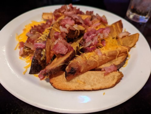 A plate of loaded potato wedges topped with melted cheese and crispy bacon bits.