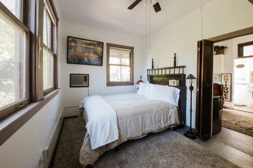Cozy bedroom with a double bed, large windows, and vintage decor, featuring a carpeted floor and an antique lamp.