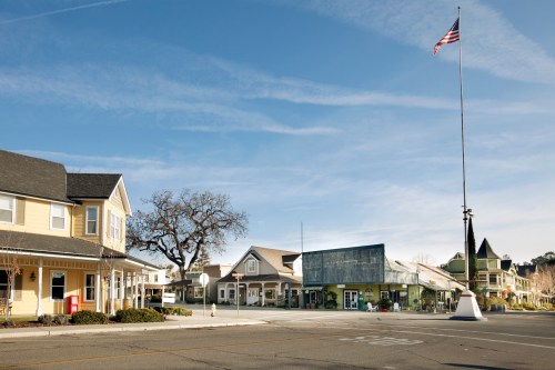 A quiet street scene featuring charming buildings, a large flagpole, and a clear blue sky.