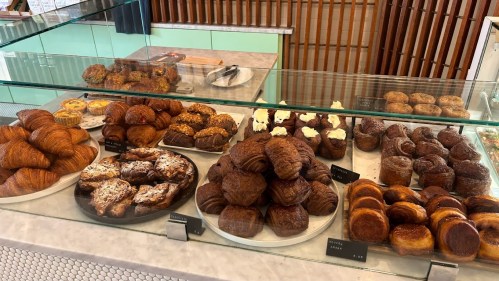A display case filled with various baked goods, including croissants, pastries, and muffins, arranged on plates.