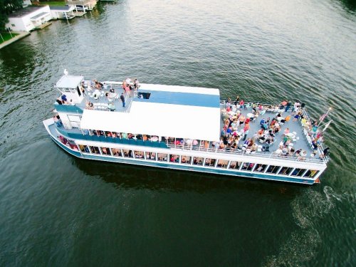 Aerial view of a large boat filled with people cruising on a calm body of water.