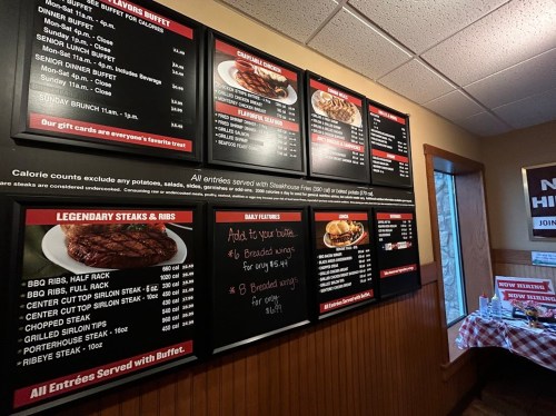 Menu board displaying various steak and rib options, prices, and buffet details in a restaurant setting.