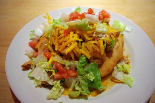 A Navajo taco, also known as a fry bread taco or Indian taco, with ground beef, cheese, lettuce, and tomatoes.
