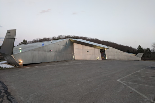 A modern, angular metal building with a sloped roof, set against a backdrop of trees and a clear sky.