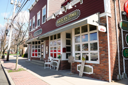 A quaint storefront with large windows, a sign reading "Back in Time," and outdoor seating on a sunny day.