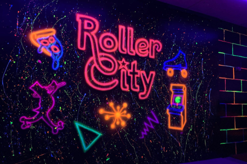 Neon sign reading "Roller City" with colorful graphics of roller skates, a unicorn, and arcade elements on a dark background.
