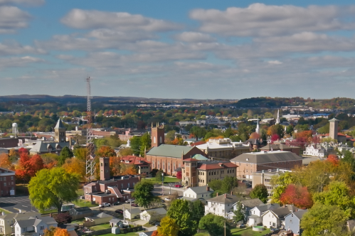 Aerial view of a town with colorful autumn trees, buildings, and a clear blue sky with clouds.