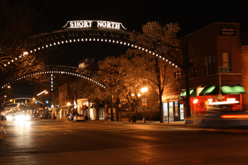 Nighttime view of Short North, featuring illuminated archway and storefronts, with light trails from passing cars.