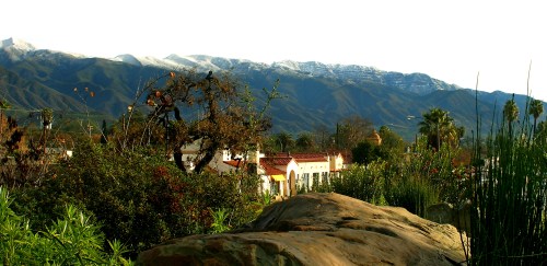 A scenic view of mountains with snow-capped peaks, lush greenery, and a charming building in the foreground.