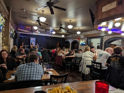 A lively restaurant scene with a crowd enjoying live music, tables filled, and food in the foreground.