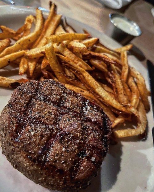 A grilled steak with a seasoned crust, served alongside crispy golden fries on a plate.